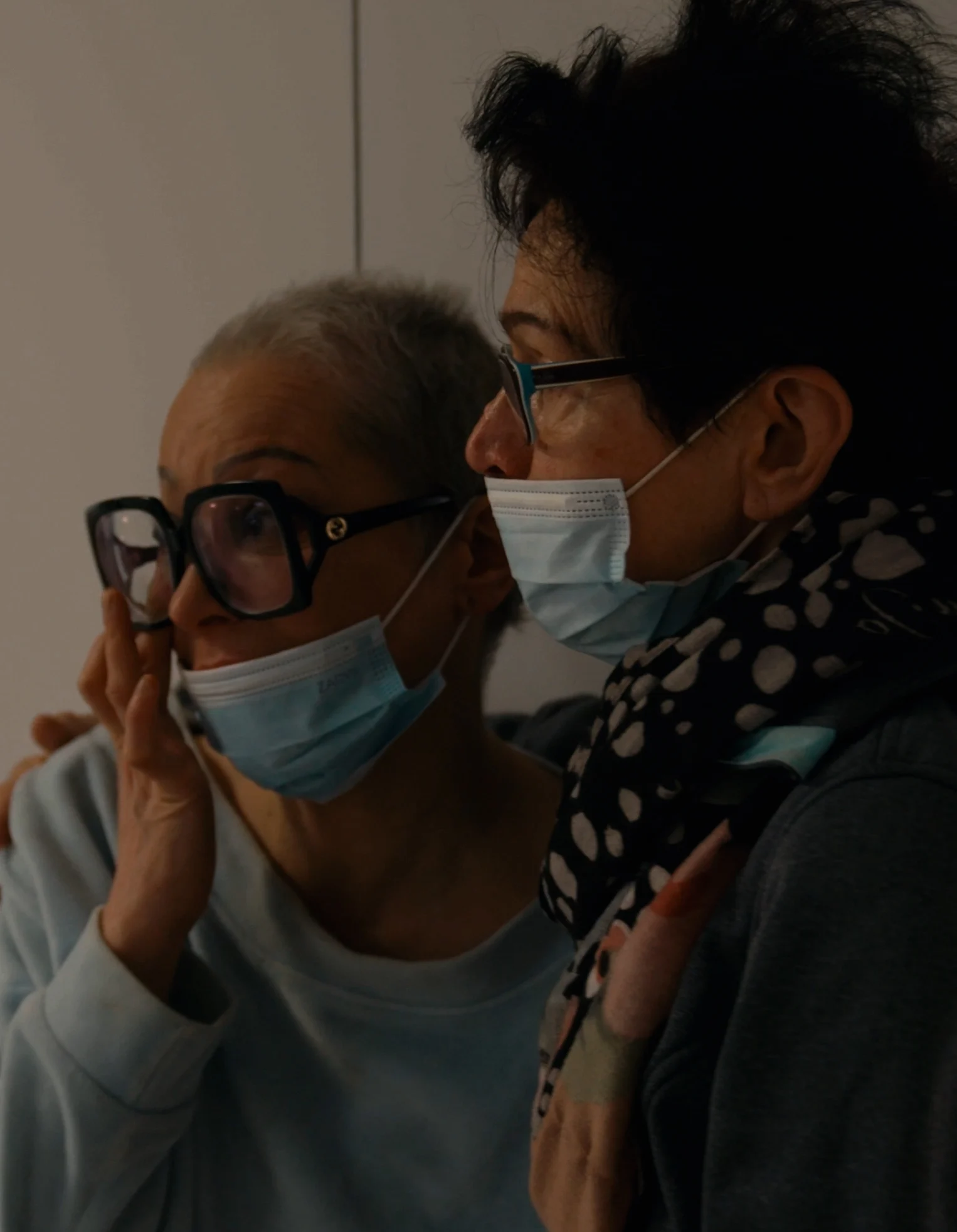 Two women in glasses, wearing masks, looking to the left