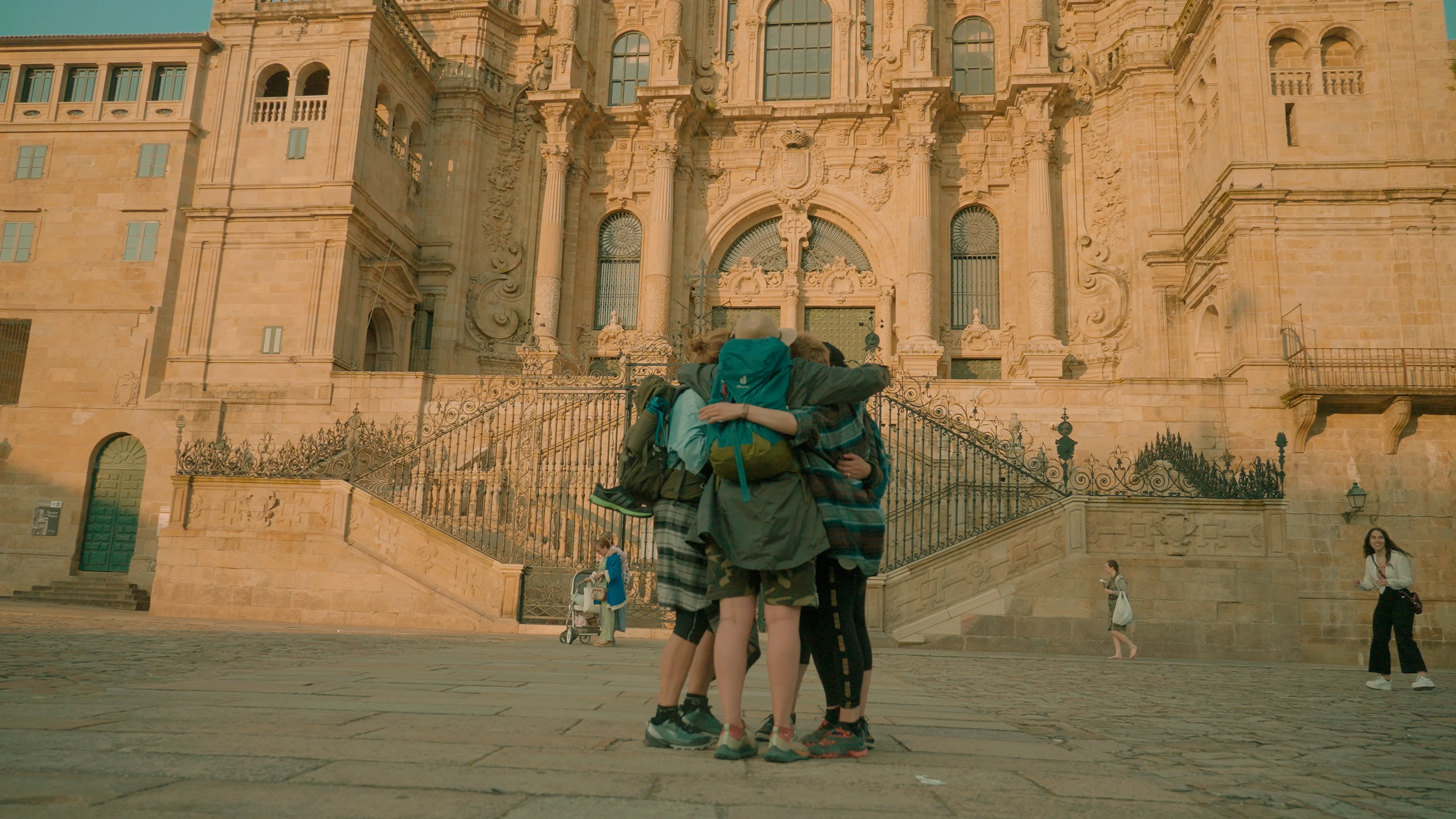 Three people hugging each other against the backdrop of a historic palace.